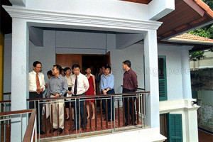 A group of formally dressed people standing on a balcony area on the second storey of a building.