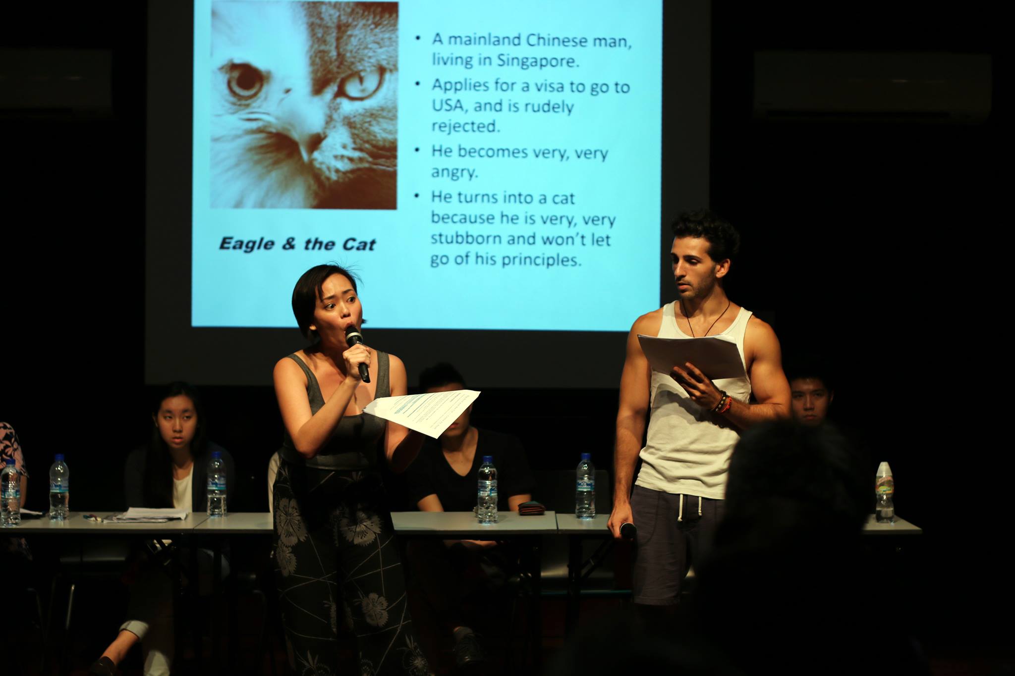 The photograph is of two performers Terri and Nathan performing a short excerpt from "The Eagle and the Cat". There is a projection of a slide in the background.