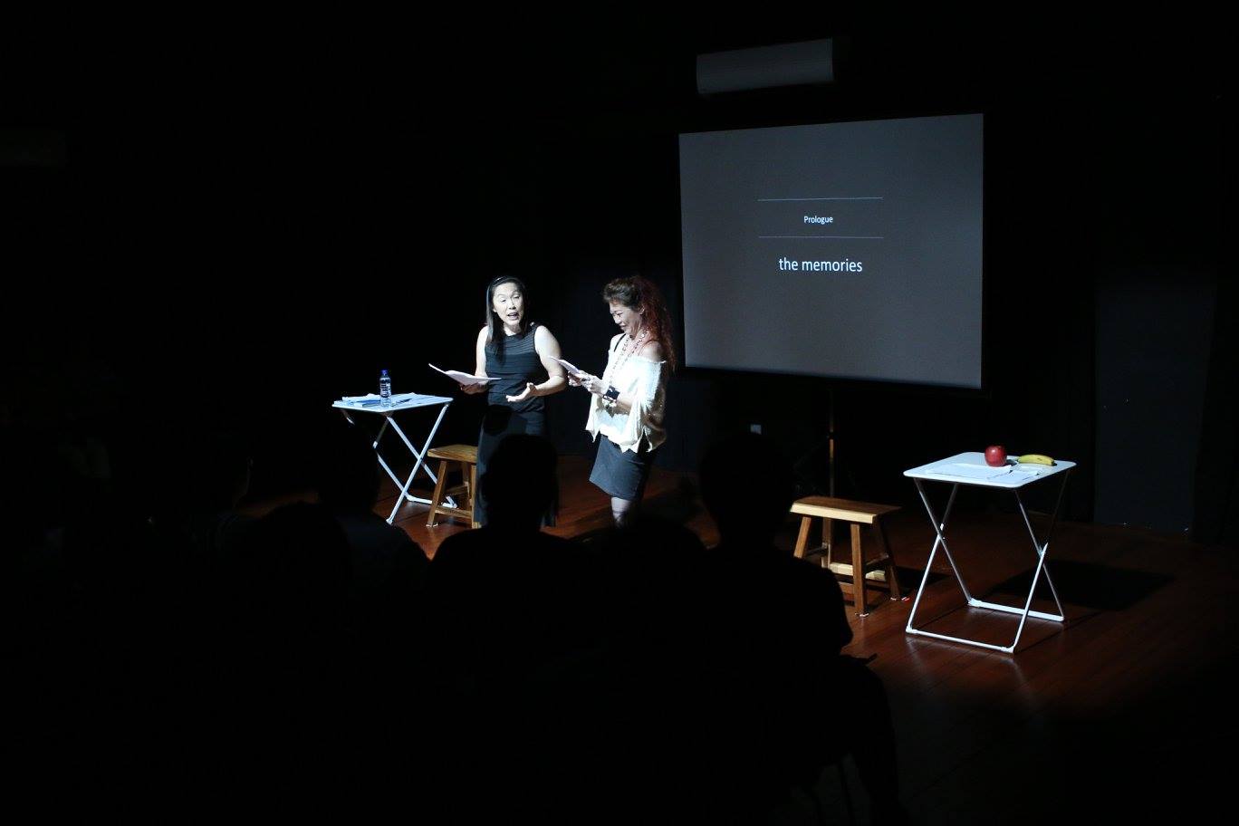 Actresses Serene Chen and Zelda Tatiana Ng on stage performing the piece. There is a screen in the background with the text 'Prologue the memories".