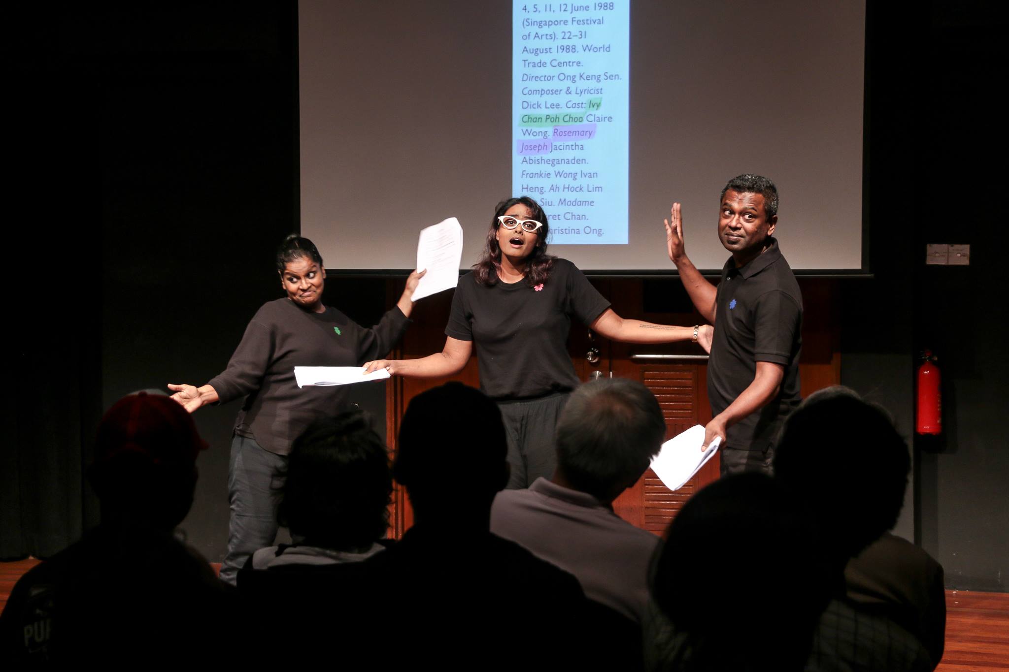 The image features three performers with various facial expressions posing in front of the audience.