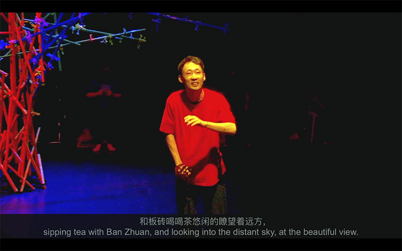 A person in a red shirt standing on a dimly lit stage, smiling as they look up. At the bottom of the image are captions in English and Chinese describing the scene.